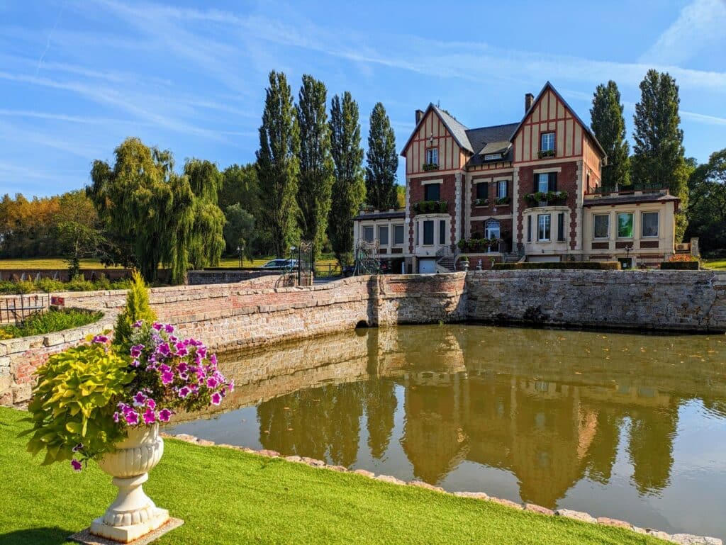 Vue du domaine avec les douves, le château et le parc boisé.
